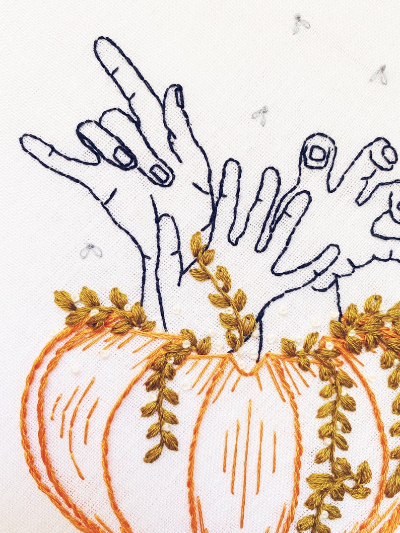 May include: Embroidered design of two hands reaching out of a pumpkin with green vines. The pumpkin is orange and the hands are black.