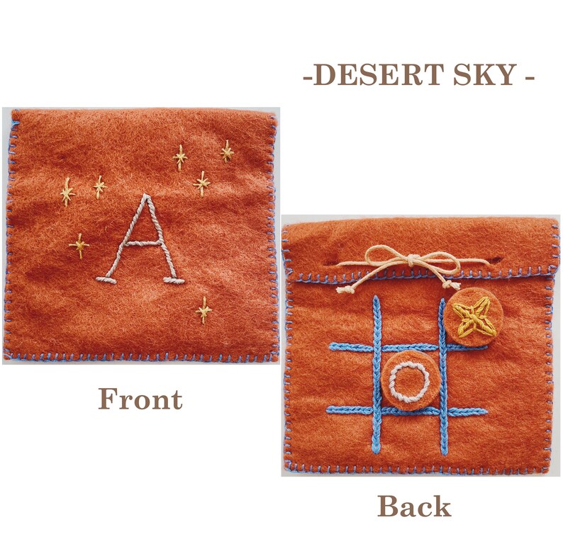May include: A felt pouch with a brown background and blue stitching. The front of the pouch has a white letter A embroidered on it with yellow stars. The back of the pouch has a tic-tac-toe board embroidered on it with a yellow star and a white circle.