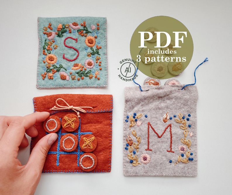 DIY Digital PDF patterns for Stitching. Three felt pouches with Hand Embroidered letters and elements. The first pouch is light blue with a floral wreath and the letter "S" in the center. The second pouch is orange with a tic-tac-toe board and nine felt circles. The third pouch is gray with a floral wreath and the letter "M" in the center.  Original MoodyGreen design, made by human