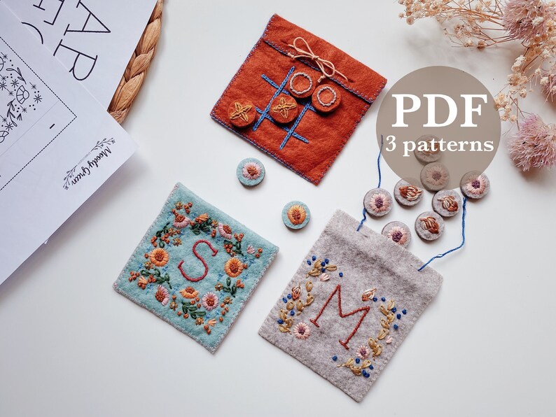 May include: Three embroidery patterns for felt pouches, including a tic-tac-toe game, a floral monogram with the letter 'S', and a floral monogram with the letter 'M'. The patterns are available as a PDF download.