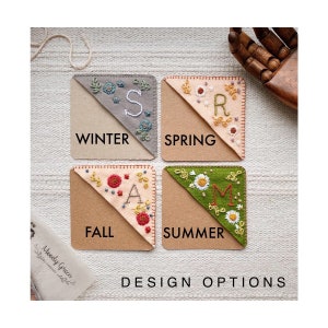 May include: Four felt corner bookmarks with embroidered floral designs and the first letter of each season: Winter (S), Spring (R), Summer (M), and Fall (A).
