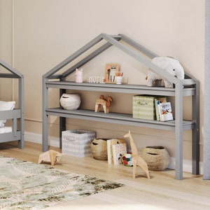 Könnte beinhalten: Ein graues, hausförmiges Bettgestell aus Holz mit einer grauen Matratze und einer braunen Decke. Das Bett steht in einem Zimmer mit einer Weltkarten-Tapete und einem grauen, hausförmigen Holzregal. Das Regal hat zwei Regalbretter und ist mit Spielzeug und Büchern gefüllt.
