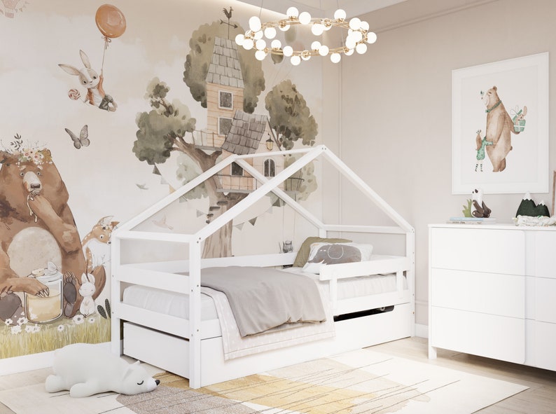May include: White wooden bed frame with a house-shaped canopy, featuring a grey and white bedding set. The bed has a pull-out drawer for storage. The room features a white dresser and a whimsical wall mural with a treehouse and animals.