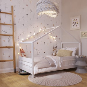 May include: White wooden bed frame with a house-shaped canopy, featuring a white and gray striped comforter, a yellow pillow, and a stuffed fox toy. The bed is decorated with string lights and a white knitted pendant light.