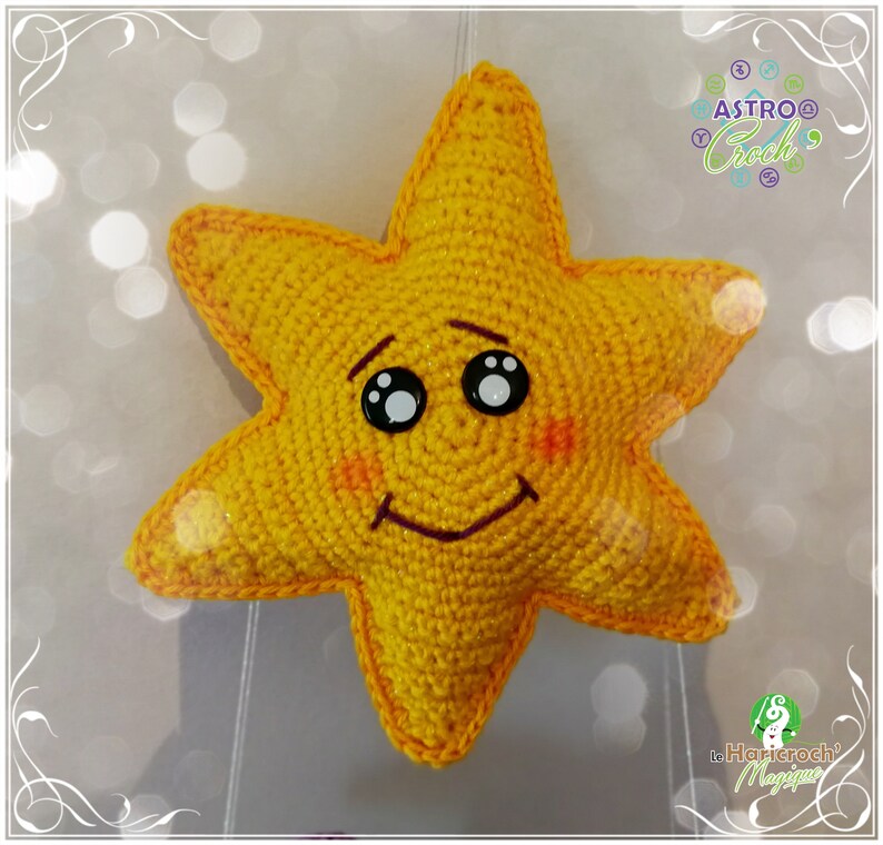 May include: A yellow crocheted star with a smiling face, black eyes, and red cheeks. The star is hanging from a string.