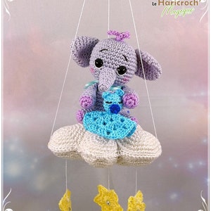 May include: A crocheted baby mobile with a purple elephant holding a blue and white crocheted teddy bear. The mobile is hanging from a white cloud with yellow stars hanging below.
