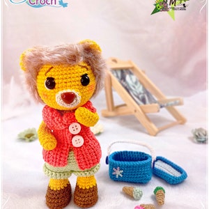 May include: A crocheted yellow lion with a red jacket, green shorts, and brown shoes. The lion is holding a blue ice cream cooler with a snowflake design. There are three ice cream cones on the ground, one pink, one green, and one blue.