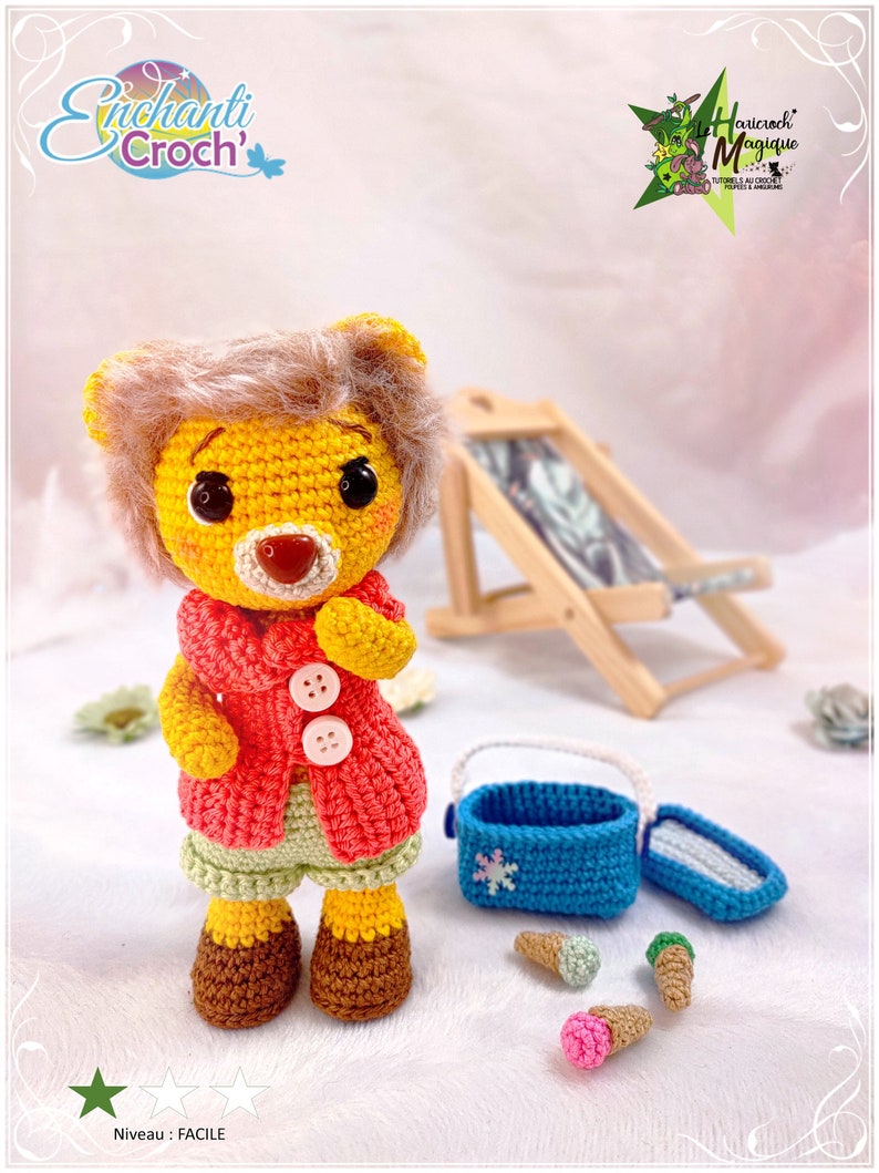 May include: A crocheted yellow lion with a red jacket, green shorts, and brown shoes. The lion is holding a blue ice cream cooler with a snowflake design. There are three ice cream cones on the ground, one pink, one green, and one blue.
