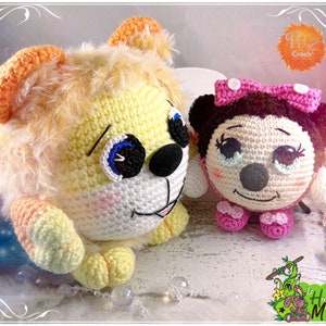 May include: Two crocheted stuffed animals, a yellow lion and a pink and black Minnie Mouse. The lion has a fluffy mane and big blue eyes. Minnie Mouse has a pink bow and a big smile.
