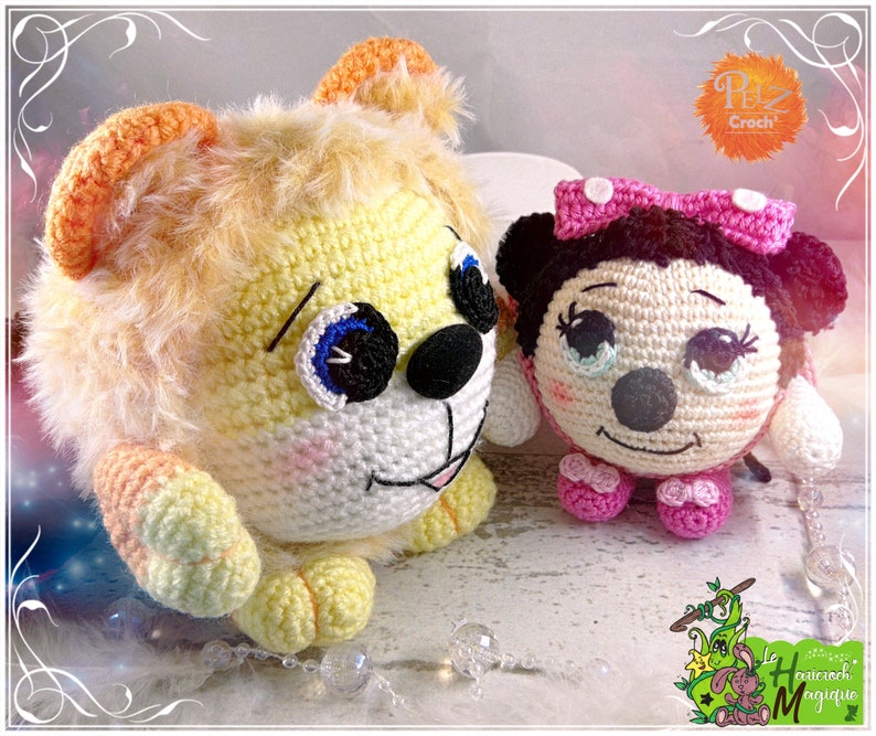 May include: Two crocheted stuffed animals, a yellow lion and a pink and black Minnie Mouse. The lion has a fluffy mane and big blue eyes. Minnie Mouse has a pink bow and a big smile.