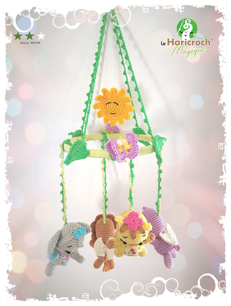 K&ouml;nnte beinhalten: Handgefertigtes Baby-Mobile aus H&auml;kelarbeit mit einer l&auml;chelnden gelben Sonne, einer lila Blume und vier entz&uuml;ckenden Tierfiguren in Grau, Braun, Gelb und Lila. Das Mobile wird von gr&uuml;nen geh&auml;kelten Kordeln gehalten und enth&auml;lt den Text "Le Haricroch' Magique".