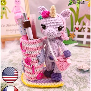 Peut inclure: Un porte-crayons en crochet en forme de licorne avec un design ray&eacute; rose et violet. La licorne a une fleur rose sur la t&ecirc;te et un sac rose. Le porte-crayons est pos&eacute; sur une base jaune.
