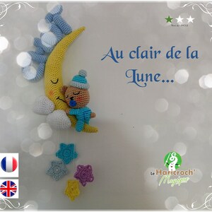 May include: A crocheted moon with a sleeping teddy bear, hanging from a white wall with blue and yellow stars. The text "Au clair de la lune..." is written in blue on the wall. The text "Le Haricroch' Magique" is written in green on the wall.