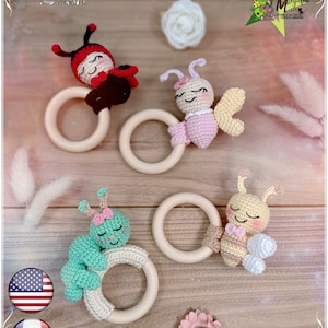 May include: Three crocheted baby teethers with wooden rings. The teethers are shaped like a ladybug, a butterfly, and a bee. The ladybug is red with black spots, the butterfly is pink with yellow wings, and the bee is yellow with black stripes. The teethers are on a wooden surface.