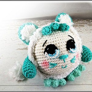 May include: A crocheted stuffed animal with a white body, teal blue accents, and a cute face. The animal has large eyes, a small nose, and a stitched smile.