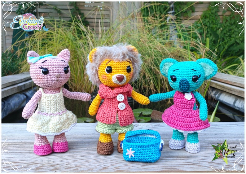 May include: Three crocheted stuffed animals: a pink cat, a yellow lion, and a blue koala. Each animal is wearing a dress and has a sweet expression. The lion is holding a blue crocheted basket.