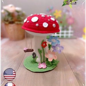 Puede incluir: Un hongo de crochet con un gorro rojo y puntos blancos, rodeado de hojas verdes y flores de colores. El hongo está sentado sobre una base verde. La imagen incluye el texto "Niveau : MOYEN" y una calificación de estrellas de tres estrellas.