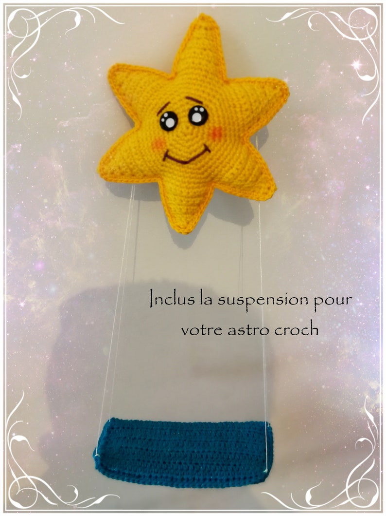 Pode incluir: Uma estrela amarela de croch&ecirc; com um rosto sorridente pendura em um barbante branco com um assento azul de croch&ecirc;. O texto "Inclus la suspension pour votre astro croch" est&aacute; escrito abaixo da estrela.