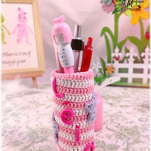 Peut inclure: Un porte-crayons en crochet ray&eacute; rose et blanc avec une figurine de poup&eacute;e rose et blanche et un stylo rouge &agrave; l'int&eacute;rieur. Le porte-crayons a un c&oelig;ur violet sur le c&ocirc;t&eacute;.