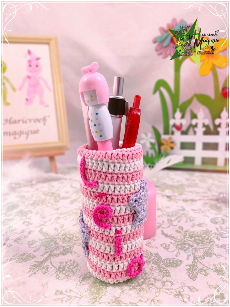 Peut inclure: Un porte-crayons en crochet ray&eacute; rose et blanc avec une figurine de poup&eacute;e rose et blanche et un stylo rouge &agrave; l'int&eacute;rieur. Le porte-crayons a un c&oelig;ur violet sur le c&ocirc;t&eacute;.