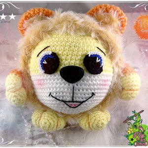 May include: A crocheted lion plush toy with a yellow and orange mane, white face, and black nose. The toy has blue eyes and a pink mouth.