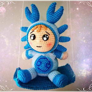 Pode incluir: Um brinquedo de pel&uacute;cia azul e branco de croch&ecirc; em forma de caranguejo. O brinquedo tem um rosto humano com olhos grandes e uma boca pequena. O brinquedo est&aacute; sentado em um balan&ccedil;o de croch&ecirc; azul.