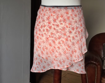 Può includere: Una gonna di chiffon bianca con stampa floreale in tonalità arancio e rosa. La gonna ha una cintura grigia e un orlo a balze.