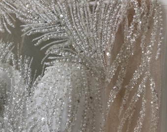 Puede incluir: Un vestido blanco de manga larga con cuello alto y diseño de cuentas. El vestido está cubierto de pequeñas cuentas y lentejuelas blancas.