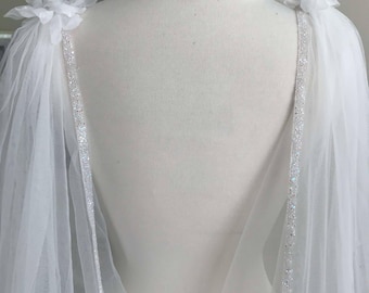 May include: White tulle bridal cape with a beaded trim and a flower detail on each shoulder.