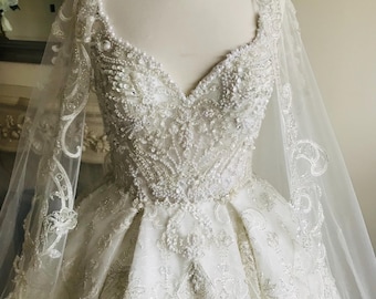 May include: A white wedding dress with a sweetheart neckline and a full skirt. The dress is embellished with beading and lace. The dress has a long train and a matching veil.