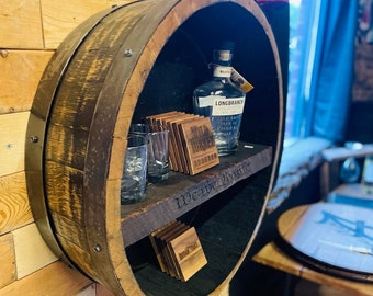 Può includere: Una mensola circolare rustica realizzata con un barile di legno riciclato. Espone una bottiglia di bourbon Longbranch, sottobicchieri Wild Turkey Bourbon e due bicchieri vuoti. La mensola è montata su una parete di legno.