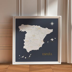 Può includere: Mappa incorniciata della Spagna con contorno bianco su sfondo blu scuro. La mappa include i nomi delle città e delle regioni in oro. La parola "ESPAÑA" è scritta in oro in basso. La cornice è bianca.