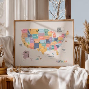 Op de afbeelding: Een ingelijste kaart van de Verenigde Staten, waarbij elke staat een andere kleur heeft. De kaart bevat illustraties van dieren en bezienswaardigheden. De woorden "my US map" staan rechtsonder. Het frame is gemaakt van lichtbruin hout.