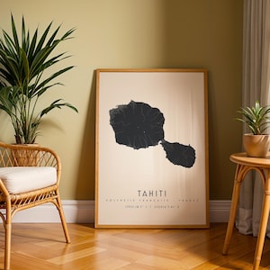 Könnte beinhalten: Ein gerahmter Druck mit einer schwarzen topografischen Karte von Tahiti auf cremefarbenem Hintergrund. Der Druck enthält das Wort "TAHITI" und Koordinaten. Der Rahmen ist aus hellem Holz. Der Druck wird in einem Raum mit einer Pflanze und einem Korbstuhl ausgestellt.