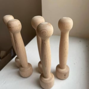 Op de afbeelding: Een verzameling onafgewerkte houten dumbbells. Elke dumbbell heeft een afgeronde handgreep en een cirkelvormige basis. De houtnerf is zichtbaar, waardoor ze een natuurlijke uitstraling hebben. Ze zijn gerangschikt op een wit oppervlak.