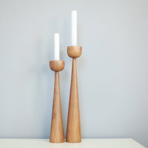 May include: Two wooden candle holders with tapered bases and rounded tops. The taller holder is on the right and the shorter holder is on the left. Both holders have white candles.
