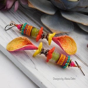 May include: A pair of handcrafted earrings featuring colorful polymer clay beads and petal-shaped dangles. The earrings showcase a vibrant mix of orange, yellow, pink, and turquoise, with intricate patterns and beadwork. The text "Designs by Alesia Dehn" is visible.