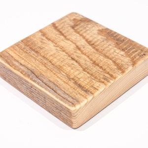 May include: A square wooden coaster with a natural wood finish. The coaster has a slightly rounded edge and a smooth surface.