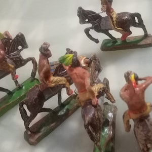 Può includere: Un set di sei miniature di guerrieri nativi americani a cavallo. Le figure sono dipinte in marrone, rosso, giallo e verde. I cavalli sono marroni e neri.
