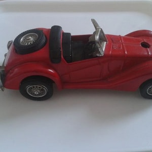 May include: A red toy car with a black convertible top and chrome wheels. The car is a classic design with a long hood and a short rear deck.