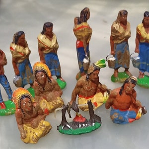 May include: A collection of 11 hand-painted figurines depicting Native American people in various poses. The figurines are made of metal and have a rustic, vintage look. Some of the figurines are holding buckets, while others are sitting around a campfire.