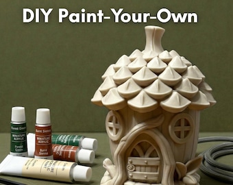 Könnte beinhalten: DIY-Mal-dein-eigenes-Feenhaus-Set. Das Set enthält ein beigefarbenes Keramikhaus mit strukturiertem Dach, Farbtuben in Grün, Braun und Creme sowie Pinsel. Der Text "DIY Paint-Your-Own" steht oben.
