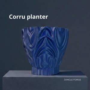 May include: A blue Corru planter with a textured, wave-like design. The planter is cylindrical with a wide opening and sits on a square base. The text "Corru planter" is at the top, and "JUNGLE FORGE" is at the bottom.