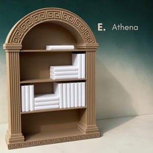 May include: A tan-colored bookshelf with a Greek key design and the text "E. Athena." The bookshelf has three shelves with stacks of white books. The top of the bookshelf has a curved arch design.
