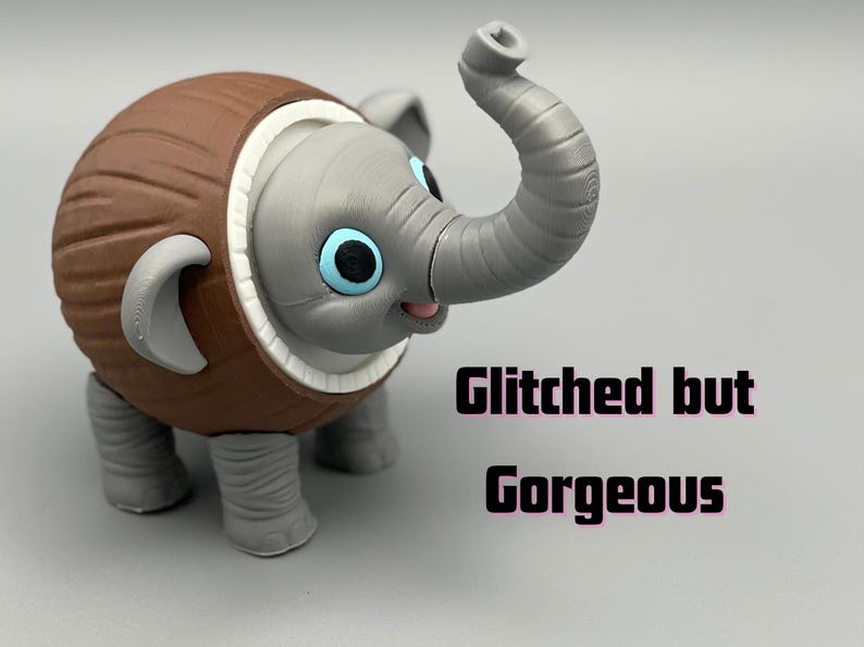 K&ouml;nnte beinhalten: Eine 3D-gedruckte Figur eines grauen Elefanten mit einem braunen, kokosnussf&ouml;rmigen K&ouml;rper, gro&szlig;en blauen Augen und einem erhobenen R&uuml;ssel. Der Text Glitched but Gorgeous ist in schwarzen Buchstaben rechts neben der Elefantenfigur aufgedruckt.