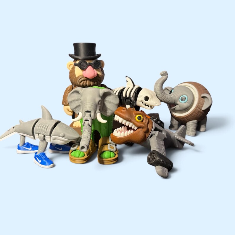 K&ouml;nnte beinhalten: Eine Sammlung kleiner Kunststofffiguren, darunter ein Hai mit blauen Turnschuhen, eine b&auml;rtige Figur mit Zylinder, ein grauer Elefant, ein Skeletthai, ein brauner Dinosaurierkopf an einem grauen Flugzeugk&ouml;rper und ein kleiner Elefant mit Kokosnuss.