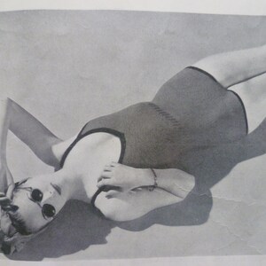 May include: A black and white photo of a person wearing a black swimsuit. The person is lying on their back with their arms above their head. The person is wearing sunglasses.