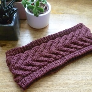 May include: A maroon knitted headband with a cable knit pattern.