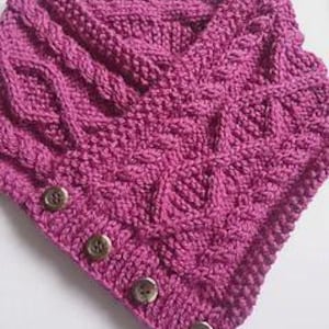 May include: A knitted purple cowl featuring a cable knit pattern and four brown buttons. The cowl is made from thick yarn and has a V-neck shape. The buttons are evenly spaced along the bottom edge.