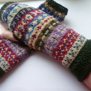 Könnte beinhalten: Handgestrickte Fingerhandschuhe mit farbenfrohem geometrischen Muster. Die Handschuhe haben Bänder in Blau, Rot, Lila und Beige, mit dunkelgrünen Bündchen. Diese Wollhandschuhe sind ideal für kalte Tage.